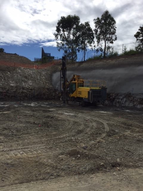 A yellow drill rig drills vertically down into the excavated pad at the Robina site, preparing the foundation for a future car park and high-rise building