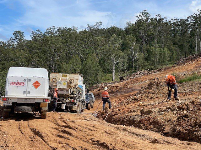 Two Beards Team members loading explosives into pre-drilled holes in Kaban Windfarm, preparing site for hard stands which will stabilize the wind turbines. An explosives truck is seen at the side on the dirt road.