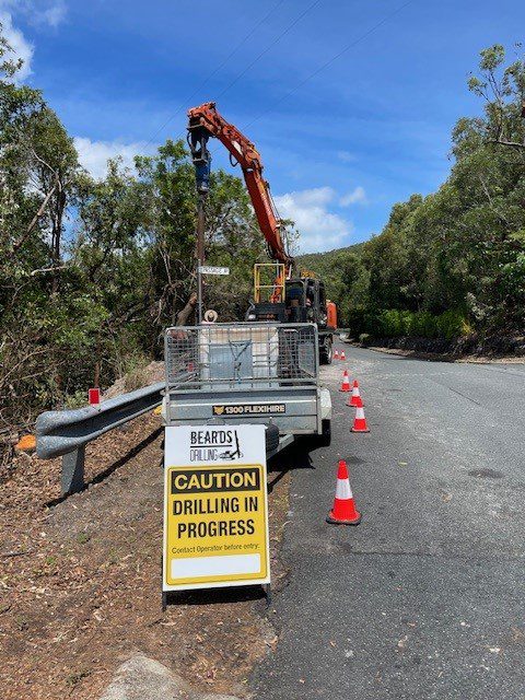 Drilling for power poles on the side of the road with machinery positioned safely and safety cones in place to allow road access